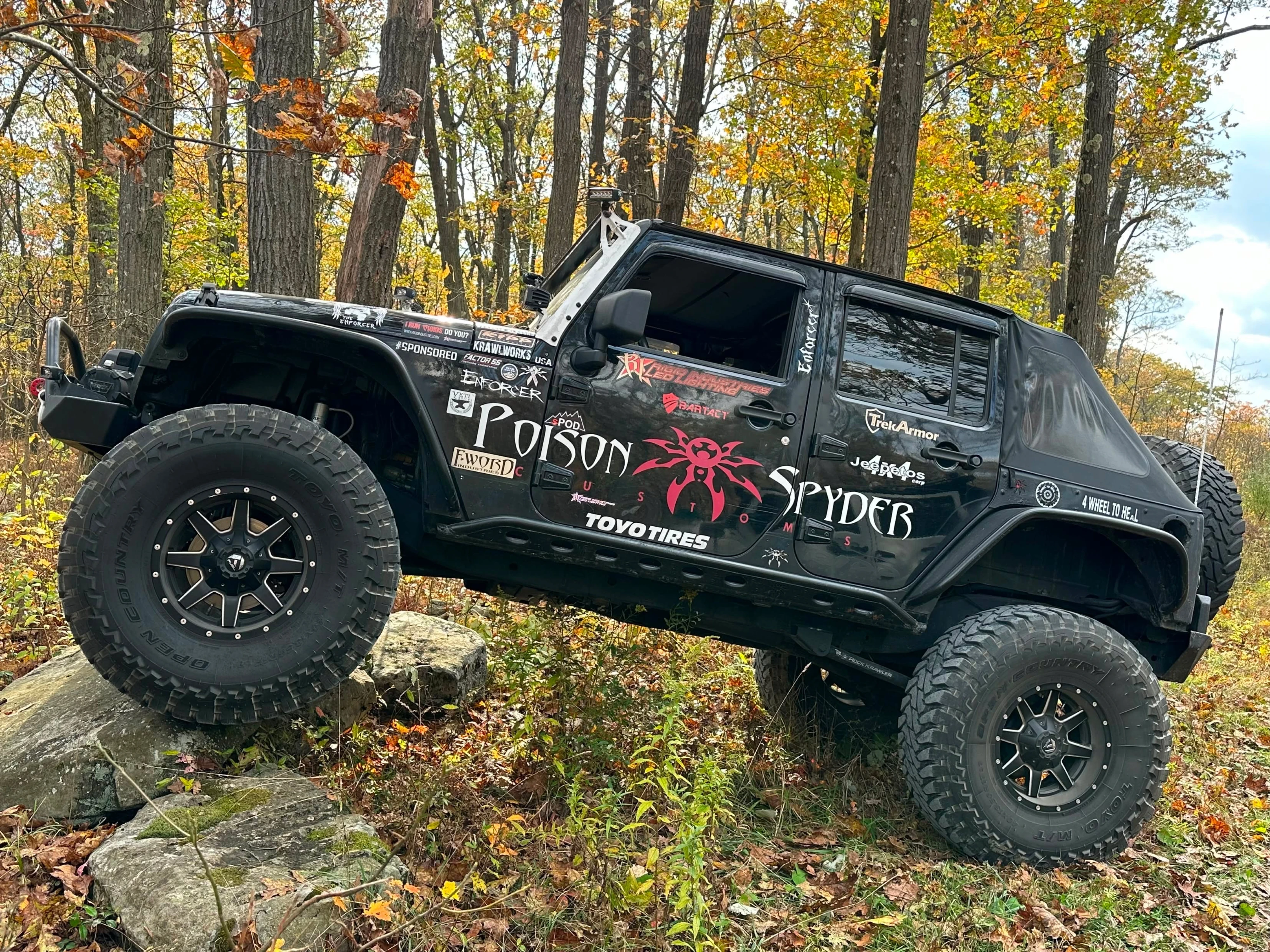 Enforcer parked on rocks in a fall forest with Poison Spyder Brawler armor and door graphics